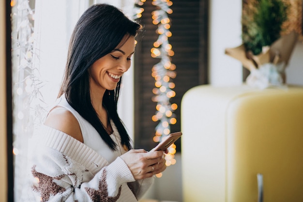 Jonge vrouw gebruikend telefoon en zich bevindt bij het venster