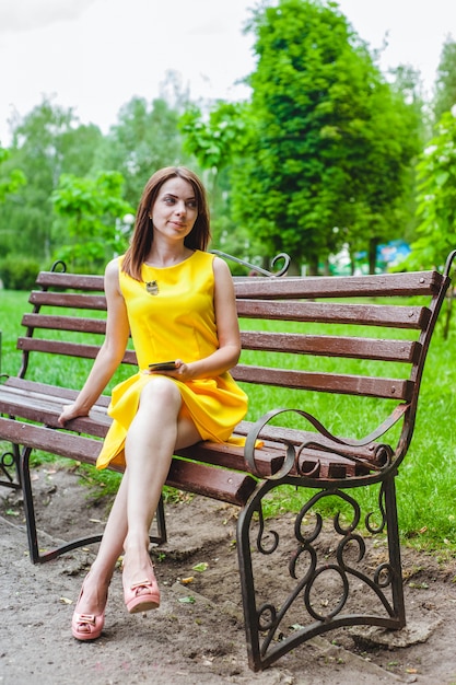 Jonge vrouw, gekleed in het geel met een slimme telefoon in haar hand