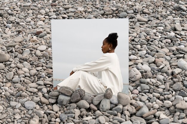 Jonge vrouw gekleed in het wit poseren met spiegel in rotsen