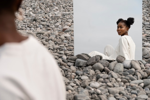 Gratis foto jonge vrouw gekleed in het wit poseren met spiegel in rotsen