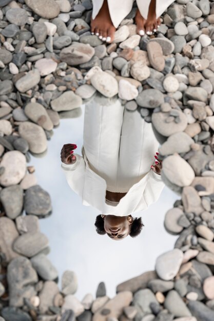 Gratis foto jonge vrouw gekleed in het wit poseren met spiegel in rotsen