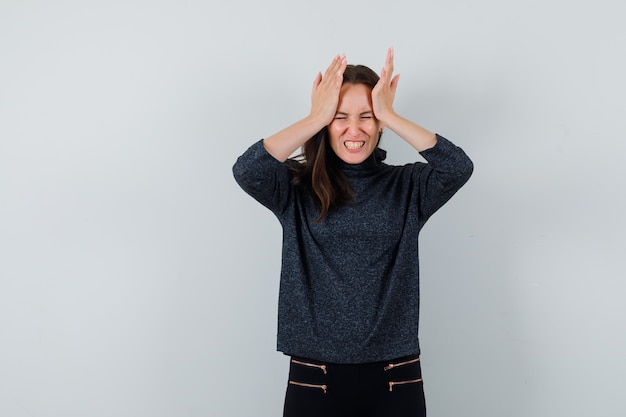 Jonge vrouw haar hoofd in zwarte blouse aan te raken en op zoek stressvol. vooraanzicht.