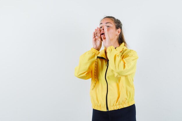 Jonge vrouw hand in hand in de buurt van mond als iemand in geel bomberjack en zwarte broek roept en er schattig uitziet