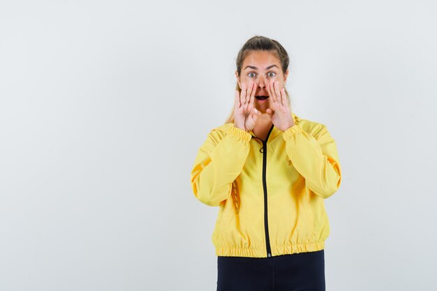 Jonge vrouw hand in hand in de buurt van mond als iemand in geel bomberjack en zwarte broek roept en er schattig uitziet