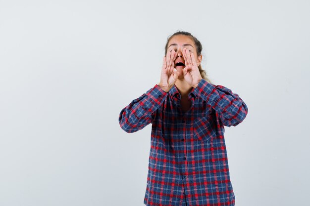 Jonge vrouw hand in hand in de buurt van mond als iemand in ingecheckte overhemd bellen en gericht kijken