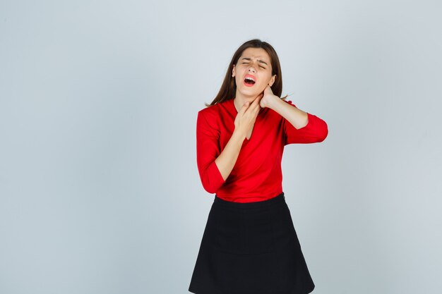 Jonge vrouw hand in hand in nek, met nekpijn in rode blouse