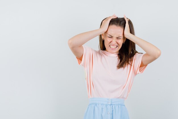 Jonge vrouw hand in hand in t-shirt, rok en op zoek geïrriteerd, vooraanzicht.