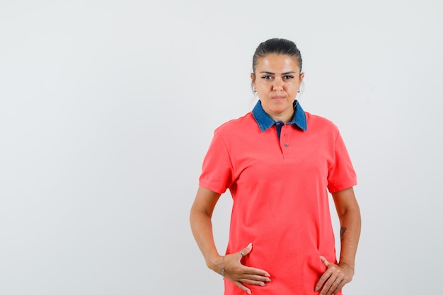 Jonge vrouw hand in hand op buik in rood t-shirt en op zoek naar ernstige, vooraanzicht.