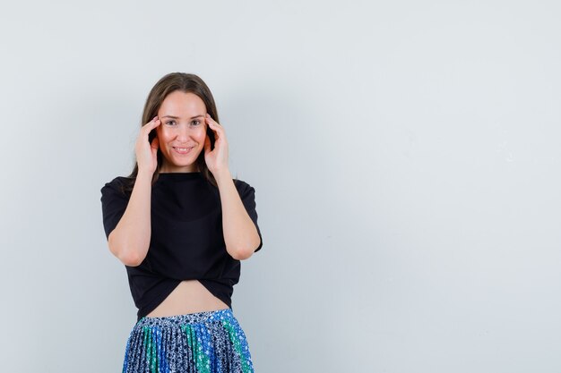 Jonge vrouw hand in hand op gezicht, gracieus glimlachend in zwart t-shirt en blauwe rok en er aantrekkelijk uitzien