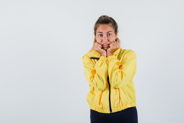 Jonge vrouw hand in hand op haar kaak in gele regenjas en op zoek verontrust