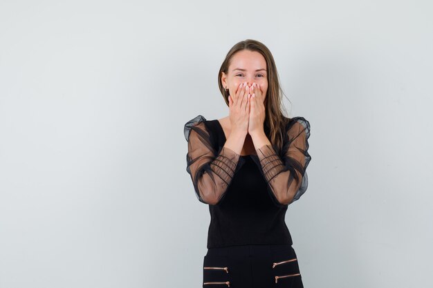 Jonge vrouw hand in hand op haar mond terwijl ze lacht in zwarte blouse en er vrolijk uitziet