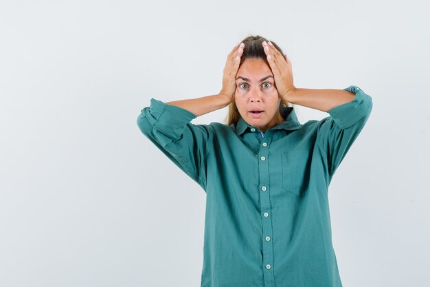 Jonge vrouw hand in hand op het hoofd in groene blouse en verrast op zoek