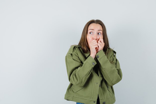 Jonge vrouw hand in hand op mond in groene jas en op zoek bang, vooraanzicht.