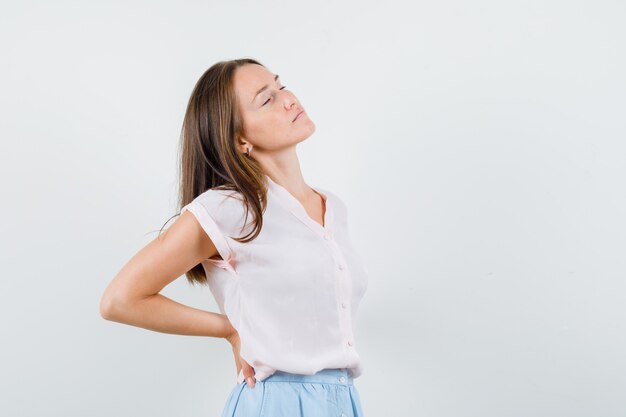 Jonge vrouw hand in hand op rug in t-shirt, rok en op zoek vredig, vooraanzicht.