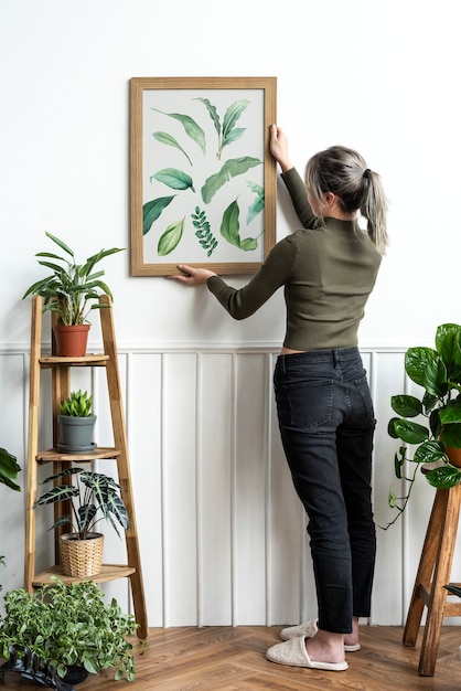 Jonge vrouw hangt een lijst van schilderij met bladprint aan de muur