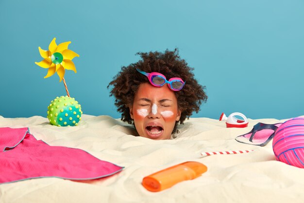 Jonge vrouw hoofd met zonnebrandcrème op gezicht omgeven door strandaccessoires