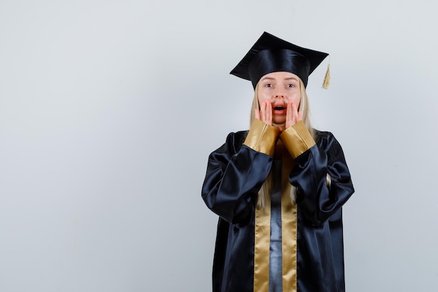 Gratis foto jonge vrouw houdt handen in de buurt van mond terwijl ze geheim vertelt in afgestudeerd uniform