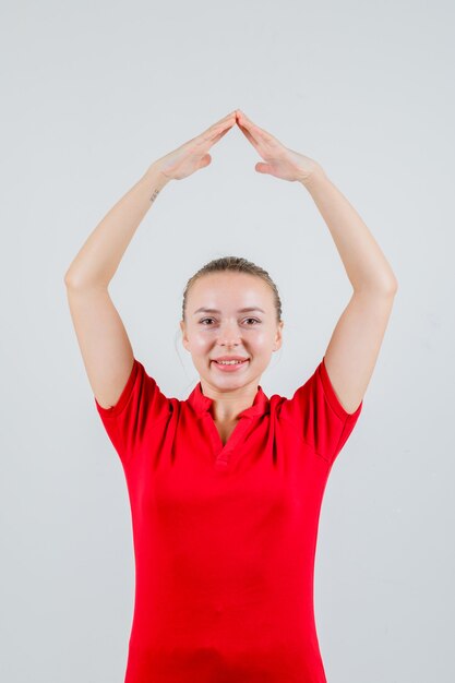 Jonge vrouw huis dak gebaar boven het hoofd in rood t-shirt maken en vrolijk kijken