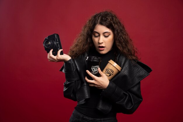 Jonge vrouw in al zwarte uitrusting die een kop en een camera houdt.