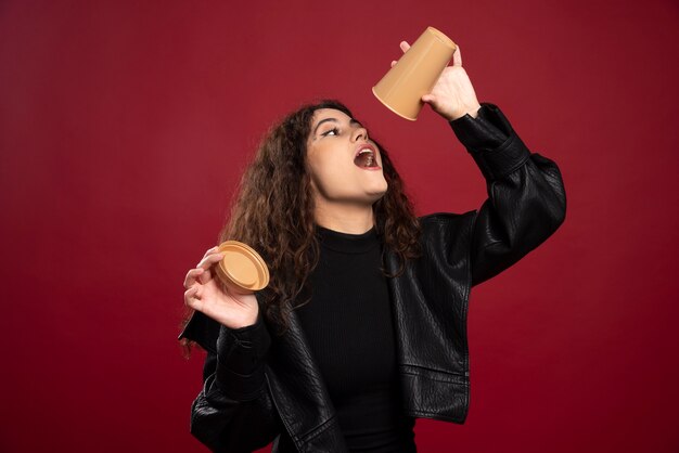 Jonge vrouw in alle zwarte outfit met geopende lege beker.