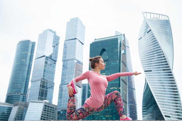 Jonge vrouw in Anjaneyasana vormen tegen de stedelijke achtergrond