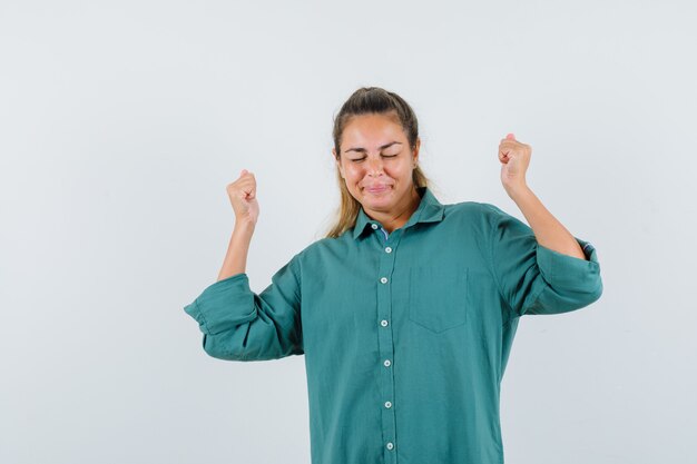 Jonge vrouw in blauw overhemd die overwinningsgebaar tonen en vrolijk kijken