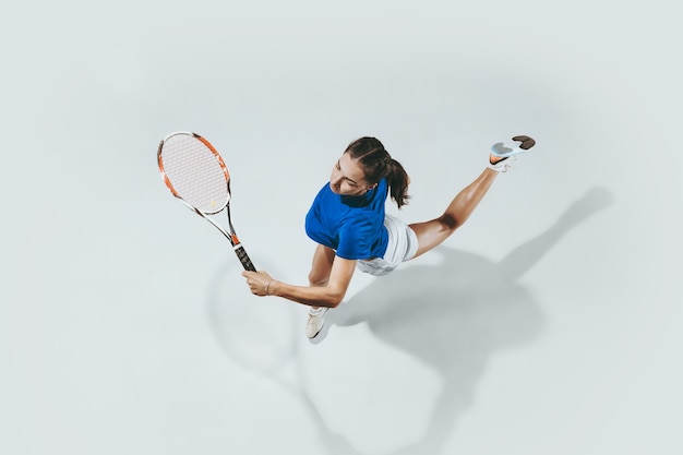 Jonge vrouw in blauw overhemd tennissen. Ze slaat de bal met een racket. Bovenaanzicht.