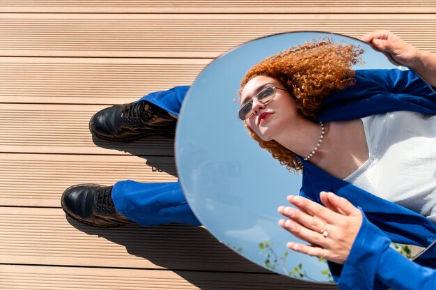 Gratis foto jonge vrouw in blauw pak poseren met spiegel buitenshuis