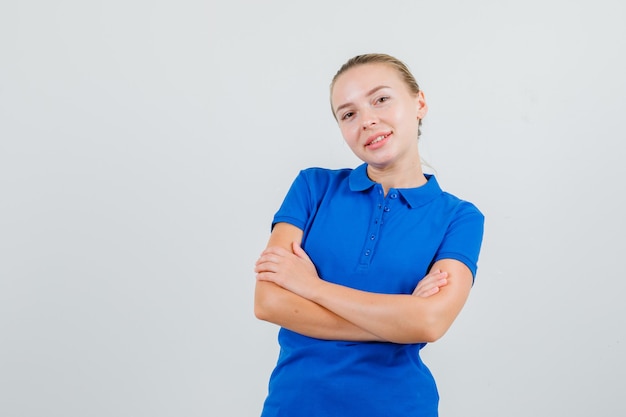 Jonge vrouw in blauw t-shirt permanent met gekruiste armen en op zoek vrolijk