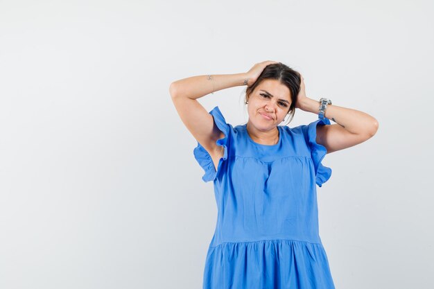 Jonge vrouw in blauwe jurk die hoofd met handen omklemt en aarzelend kijkt