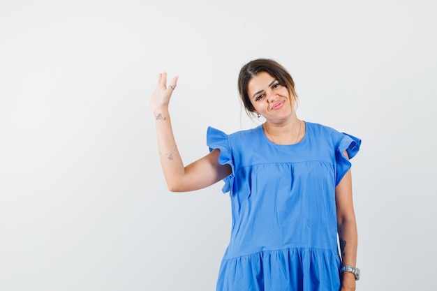 Jonge vrouw in blauwe jurk die met de hand zwaait om afscheid te nemen en er vrolijk uitziet