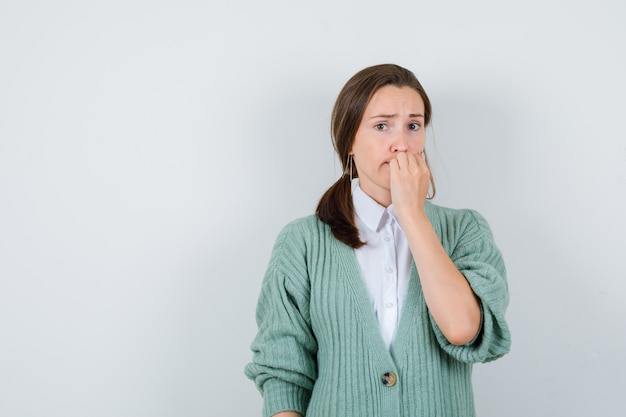 Jonge vrouw in blouse, vest bijt nagels en kijkt bezorgd, vooraanzicht.