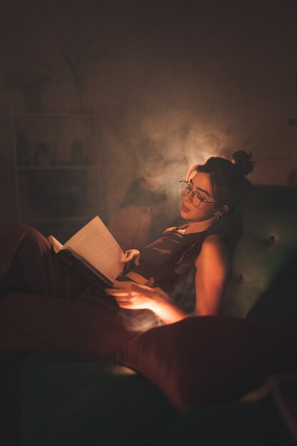 Jonge vrouw in bril die een boek leest in een gezellige woonkamer