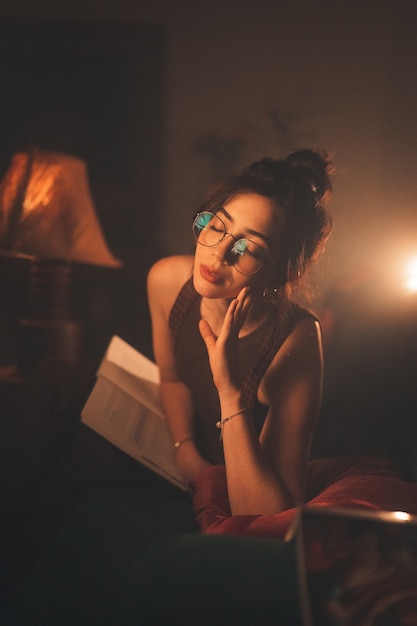 Jonge vrouw in bril die een boek leest in een gezellige woonkamer