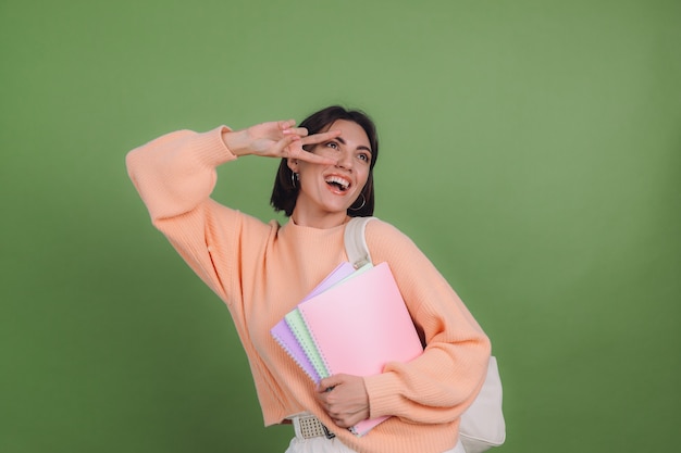 Jonge vrouw in casual perzik trui en rugzak geïsoleerd op groene olijf kleur muur