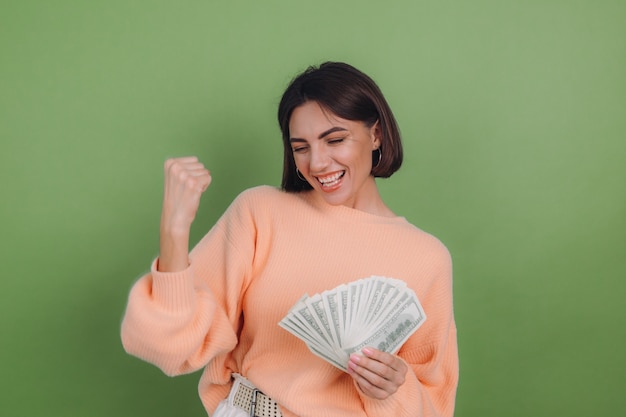 Jonge vrouw in casual perziksweater die op groene olijfmuur wordt geïsoleerd