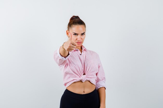 Jonge vrouw in casual shirt, broek duim opdagen en op zoek trots, vooraanzicht.