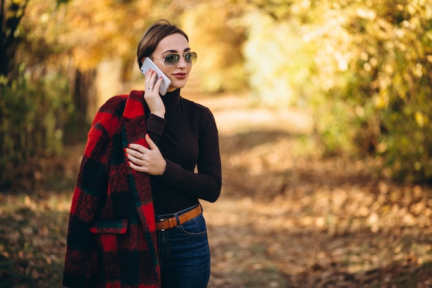 Jonge vrouw in de herfstpark die telefoon met behulp van