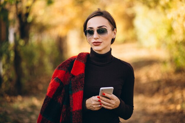 Jonge vrouw in de herfstpark die telefoon met behulp van