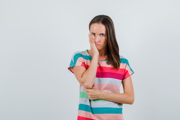 Jonge vrouw in de palm van de t-shirtholding op wang en op zoek somber, vooraanzicht.