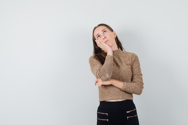 Jonge vrouw in denken pose in goud vergulde trui en zwarte broek en op zoek peinzende, vooraanzicht.