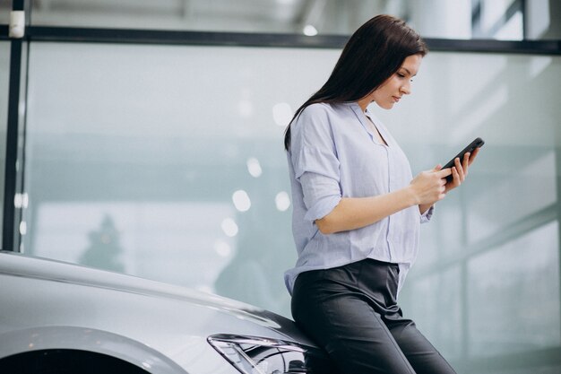 Jonge vrouw in een autoshowruimte die telefoon met behulp van