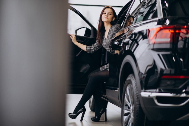 Jonge vrouw in een autotoonzaal die een auto kiest