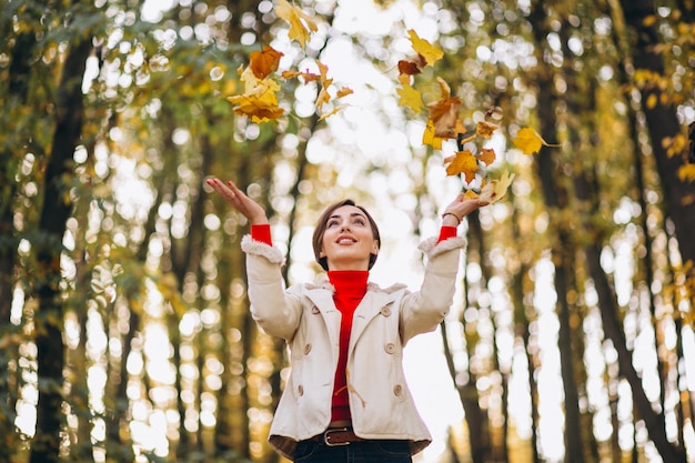 Gratis foto jonge vrouw in een de herfstpark die bladeren werpen