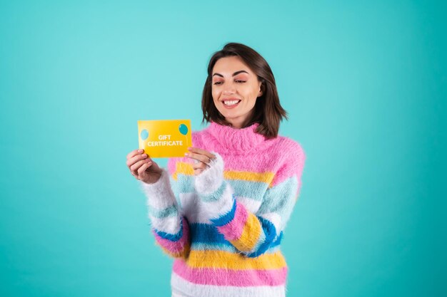 Jonge vrouw in een felgekleurde trui op blauw heeft een cadeaubon