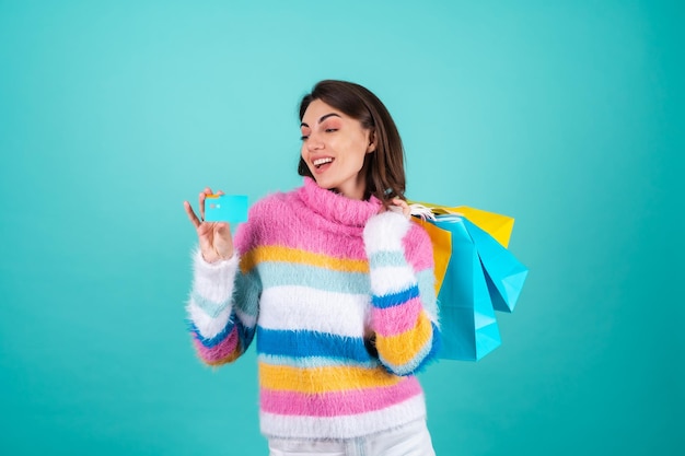 Jonge vrouw in een felgekleurde trui op blauw heeft een creditcard en boodschappentassen