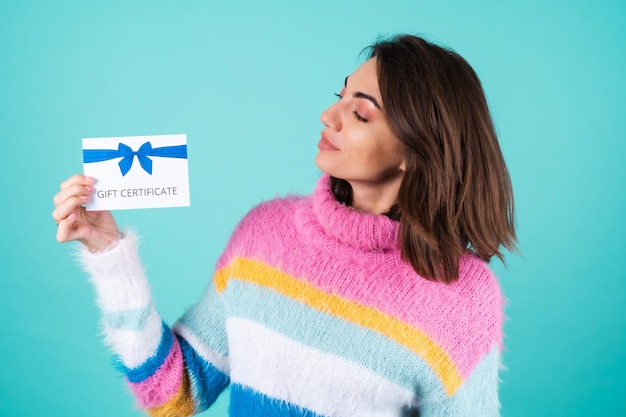 Gratis foto jonge vrouw in een felgekleurde trui op blauw met een cadeaubon