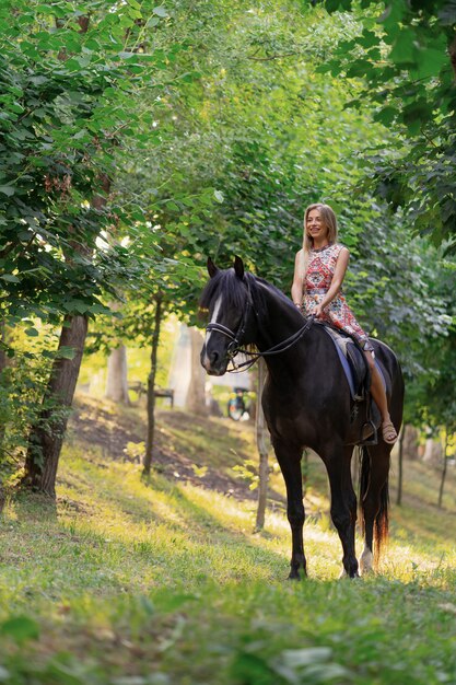 Jonge vrouw in een heldere kleurrijke kleding die een zwart paard berijdt