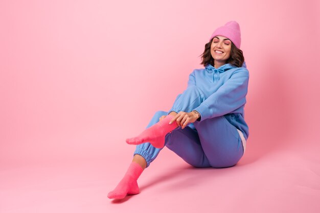 Jonge vrouw in een knus pak op fleece, een hoodie en broek, op roze, een gebreide muts op haar hoofd