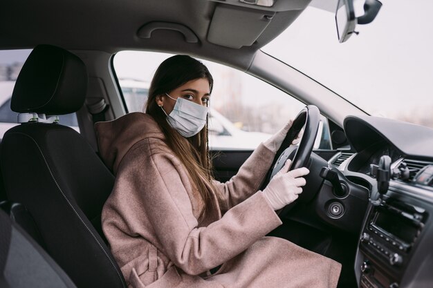 Jonge vrouw in een masker en handschoenen die een auto drijven.